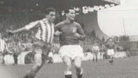 Fotografía histórica en blanco y negro de un partido entre el Real Oviedo y el Sporting de Gijón, con dos futbolistas disputando el balón.
