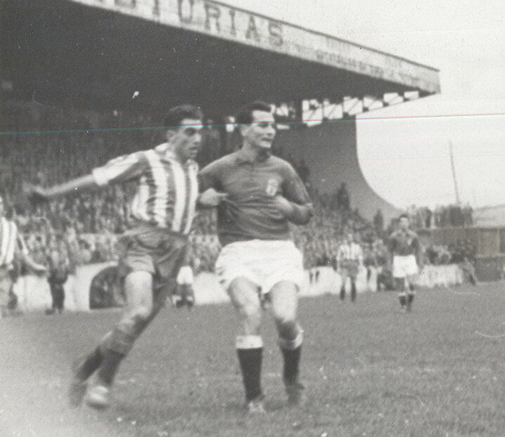 Fotografía histórica en blanco y negro de un partido entre el Real Oviedo y el Sporting de Gijón, con dos futbolistas disputando el balón.